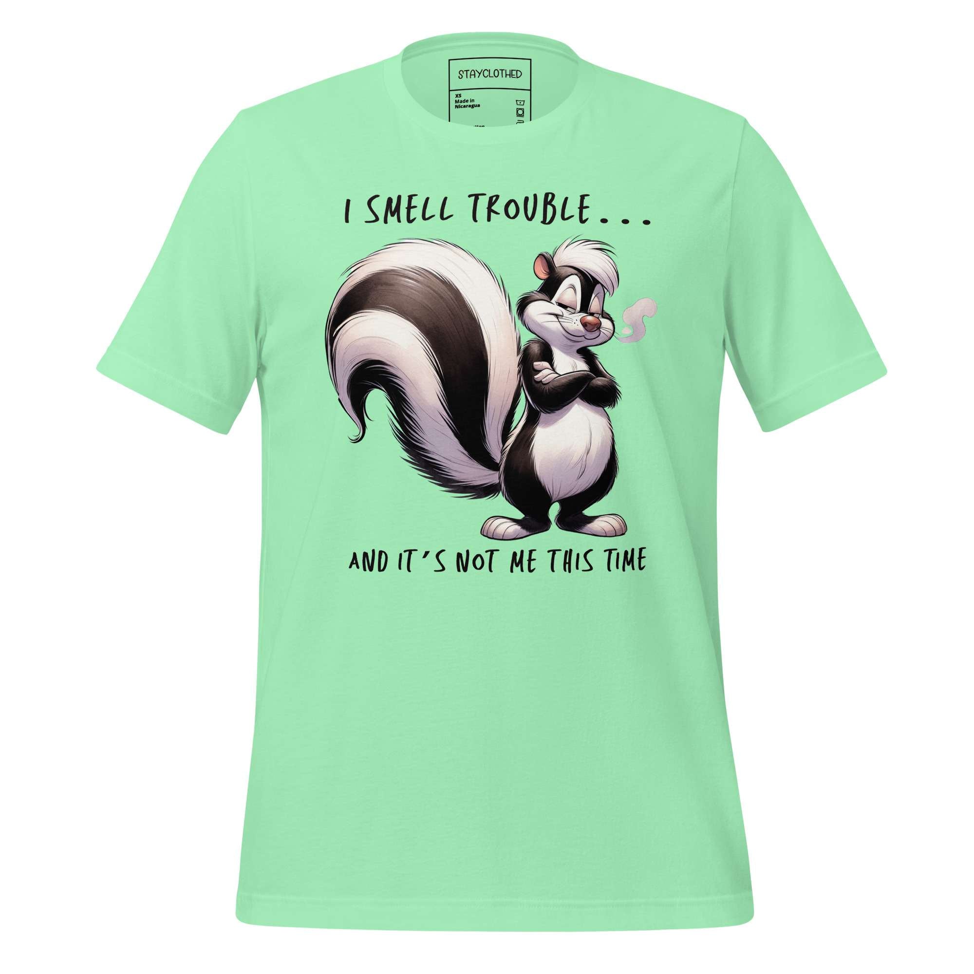 Light green t-shirt with cartoon skunk design on a wooden surface, featuring the brand 'StayClothed'.