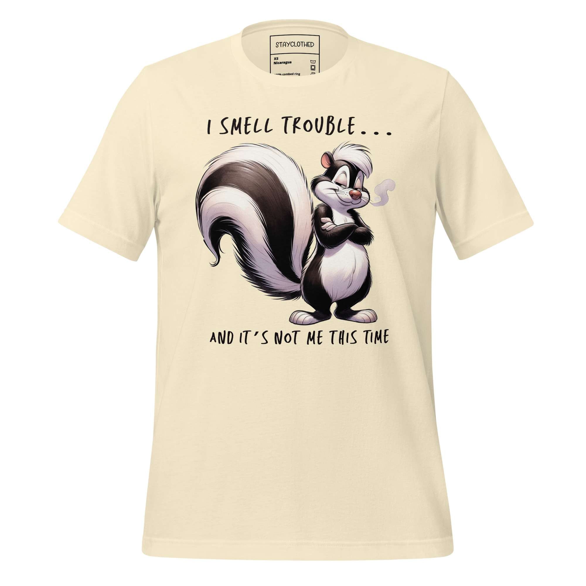 Beige t-shirt with cartoon skunk design and text on a wooden surface, featuring 'StayClothed' brand.