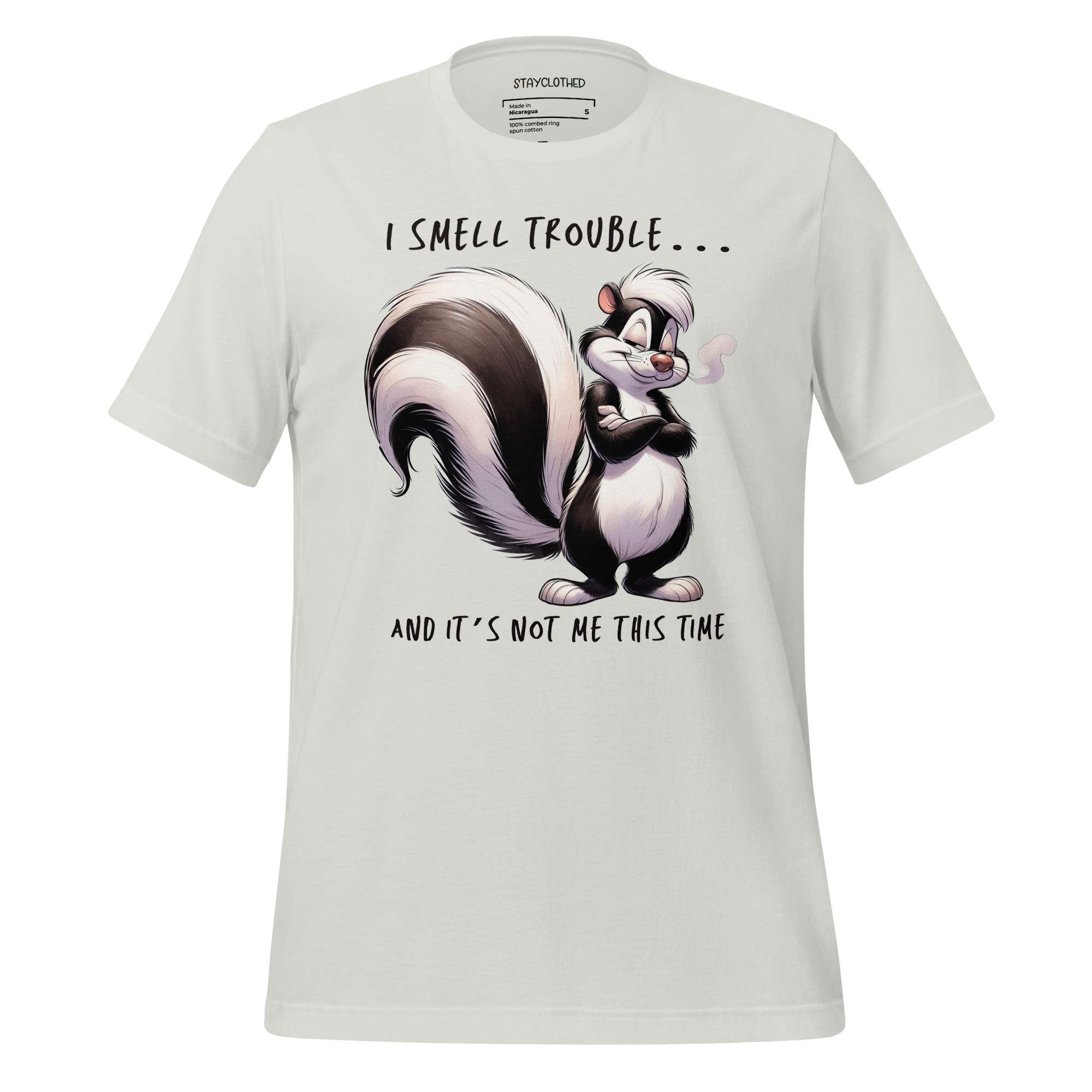 White t-shirt with a cartoon skunk design and text on a wooden surface, featuring the brand 'StayClothed'.