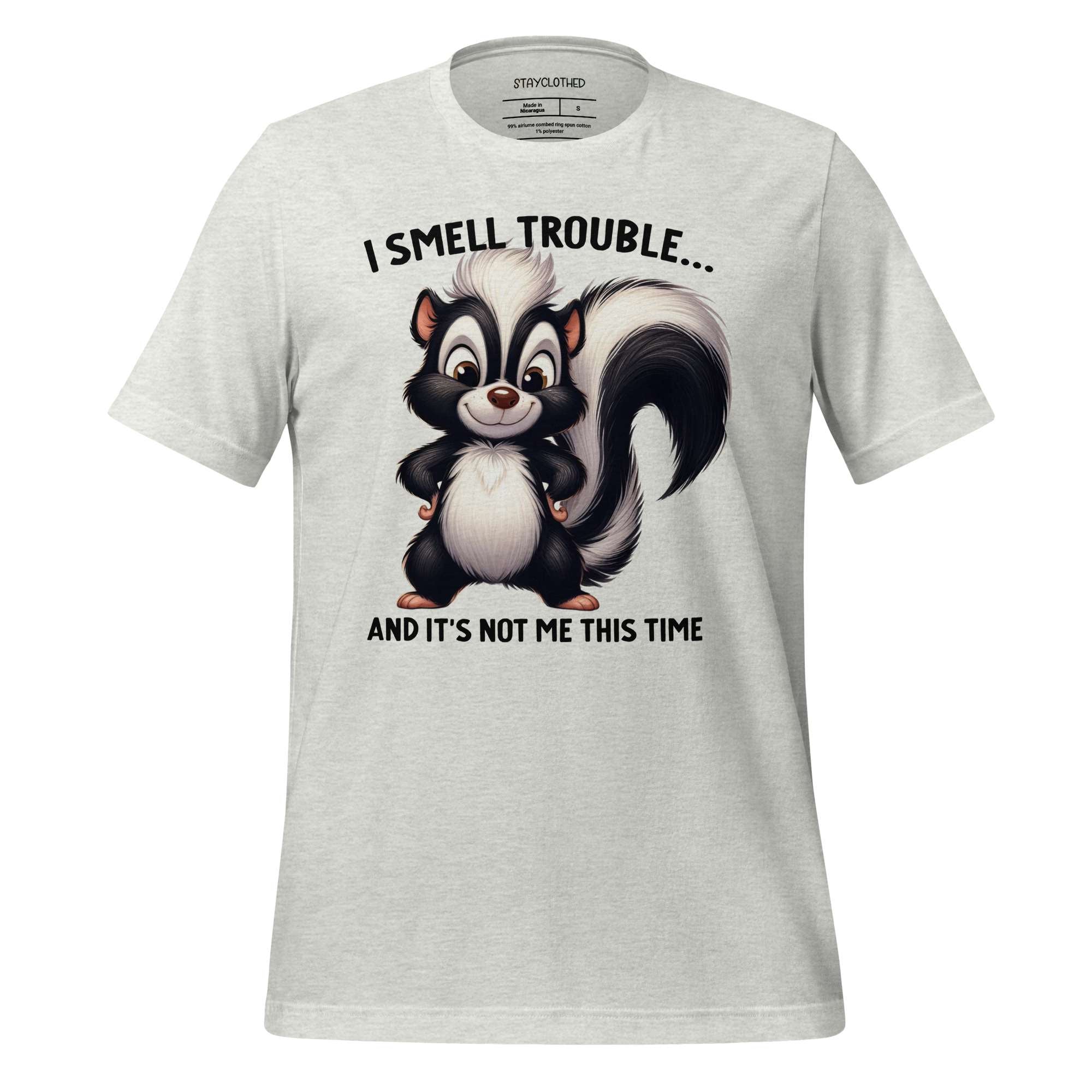 White t-shirt with cartoon skunk graphic and text on a wooden surface, featuring the brand 'StayClothed'.