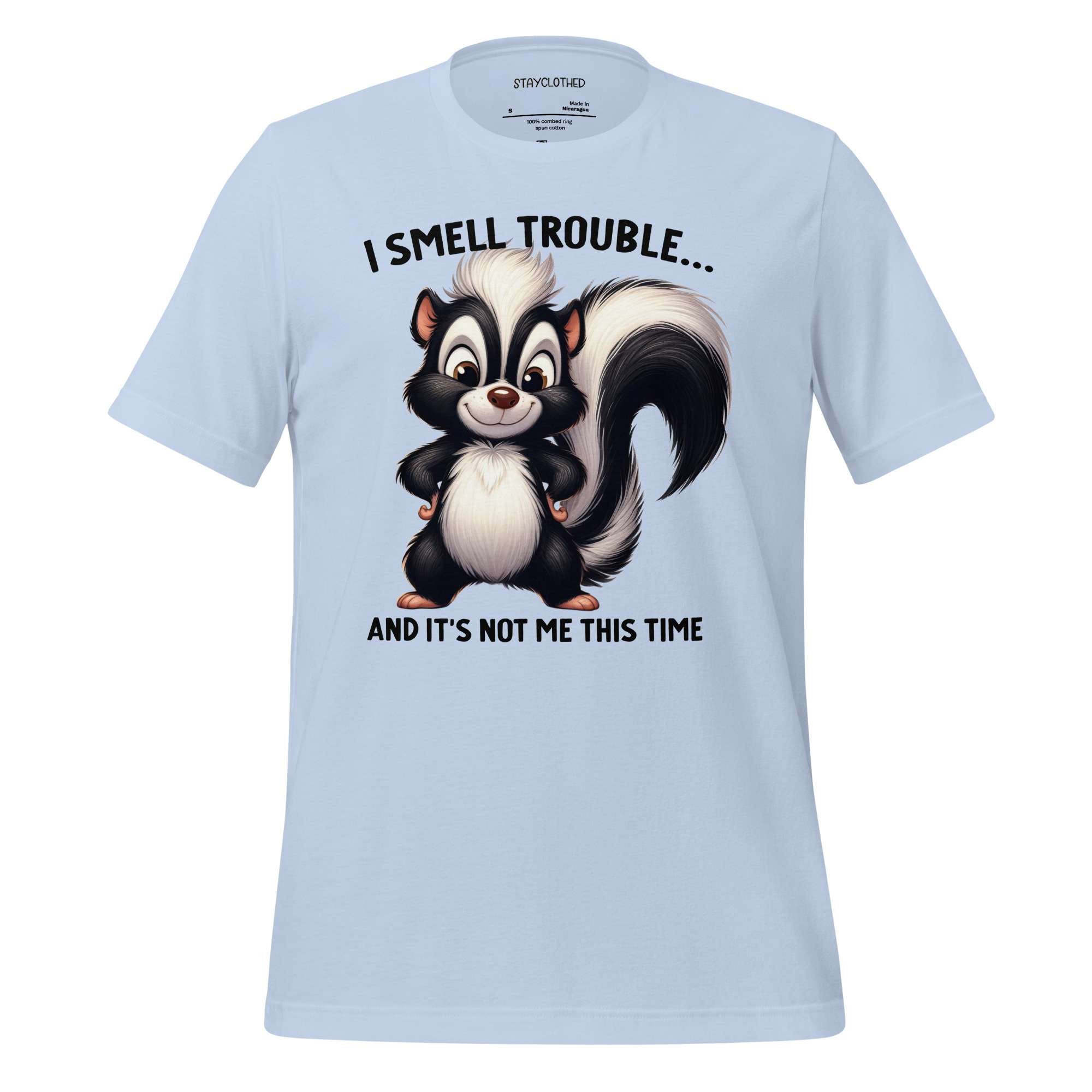 White t-shirt with a cartoon skunk graphic and text on a wooden surface, featuring the brand 'StayClothed'.