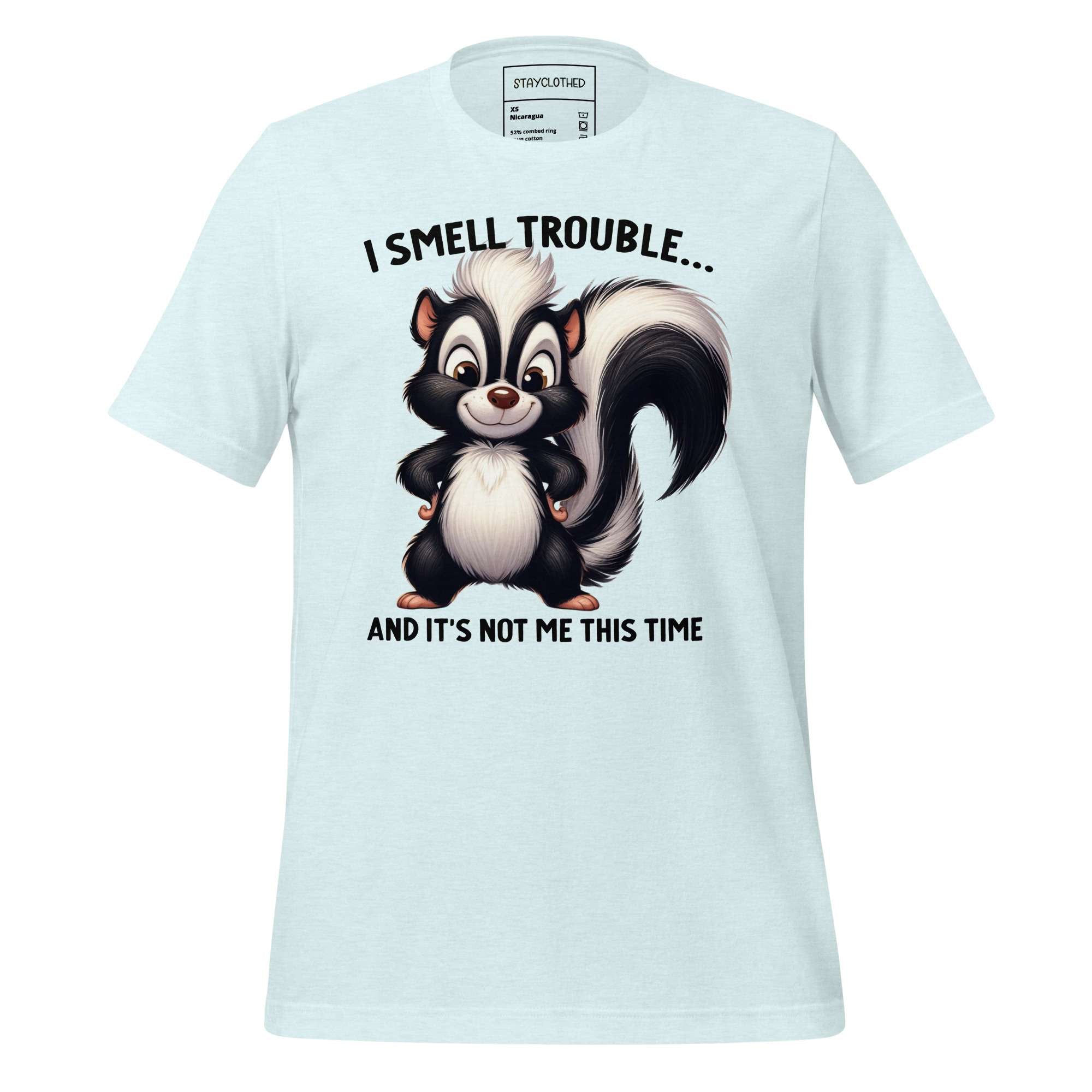 White t-shirt with cartoon skunk design and text on a wooden surface, featuring the brand 'StayClothed'.