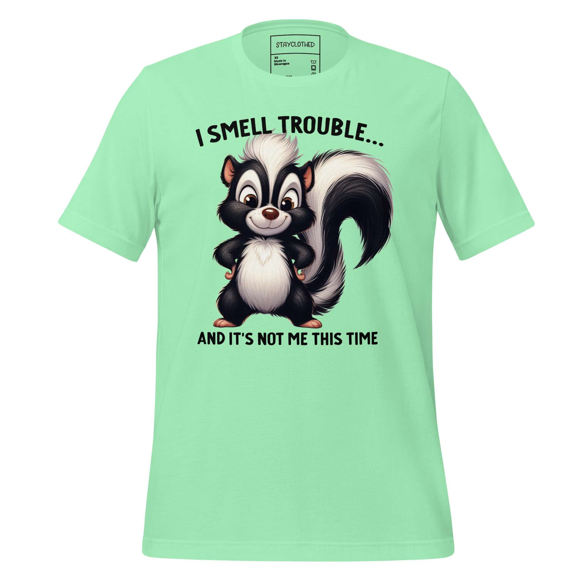 Light green t-shirt with a cartoon skunk graphic and text on a wooden surface, featuring the brand 'StayClothed'.