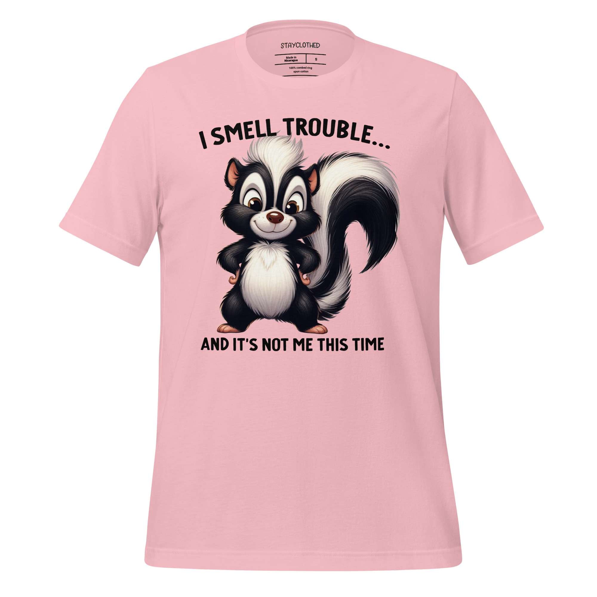 Pink t-shirt with a cartoon skunk graphic and text on a wooden surface, featuring the brand 'StayClothed'.