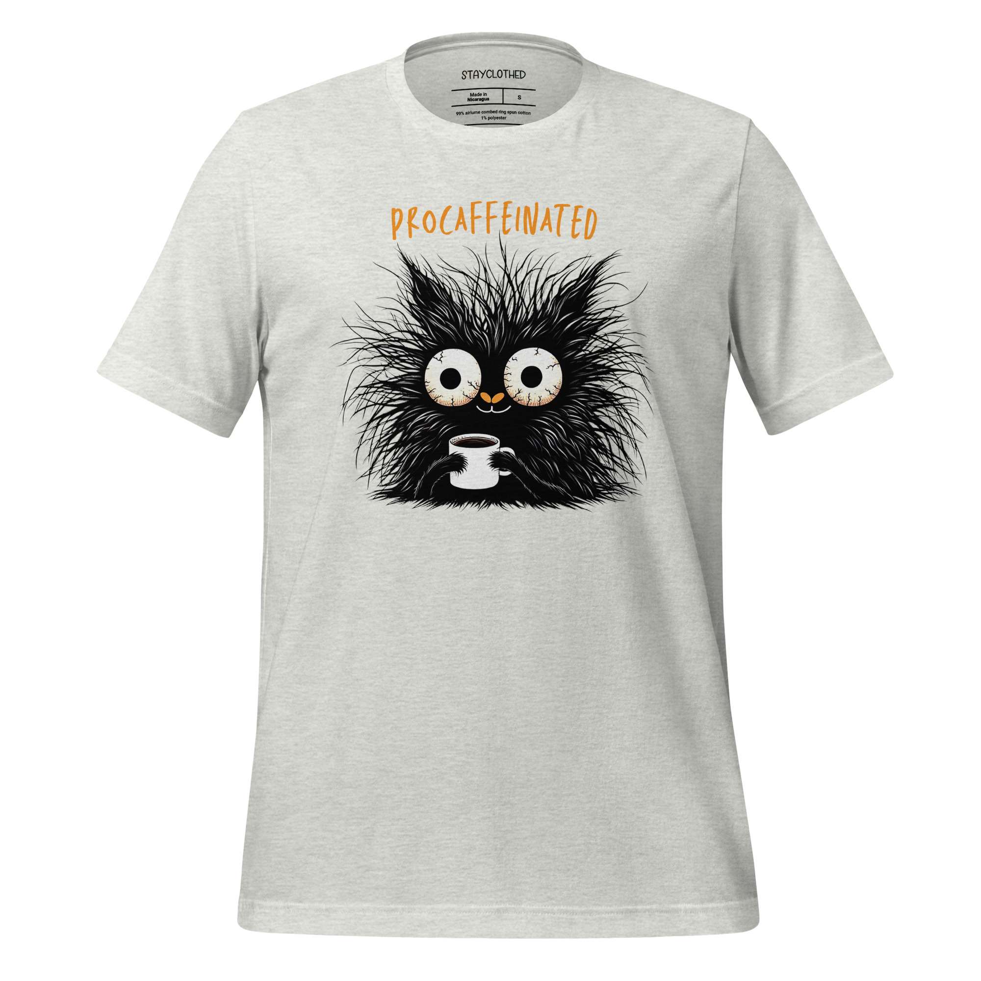 White t-shirt with a black creature holding a coffee cup graphic on a wooden surface, featuring the brand 'StayClothed'.