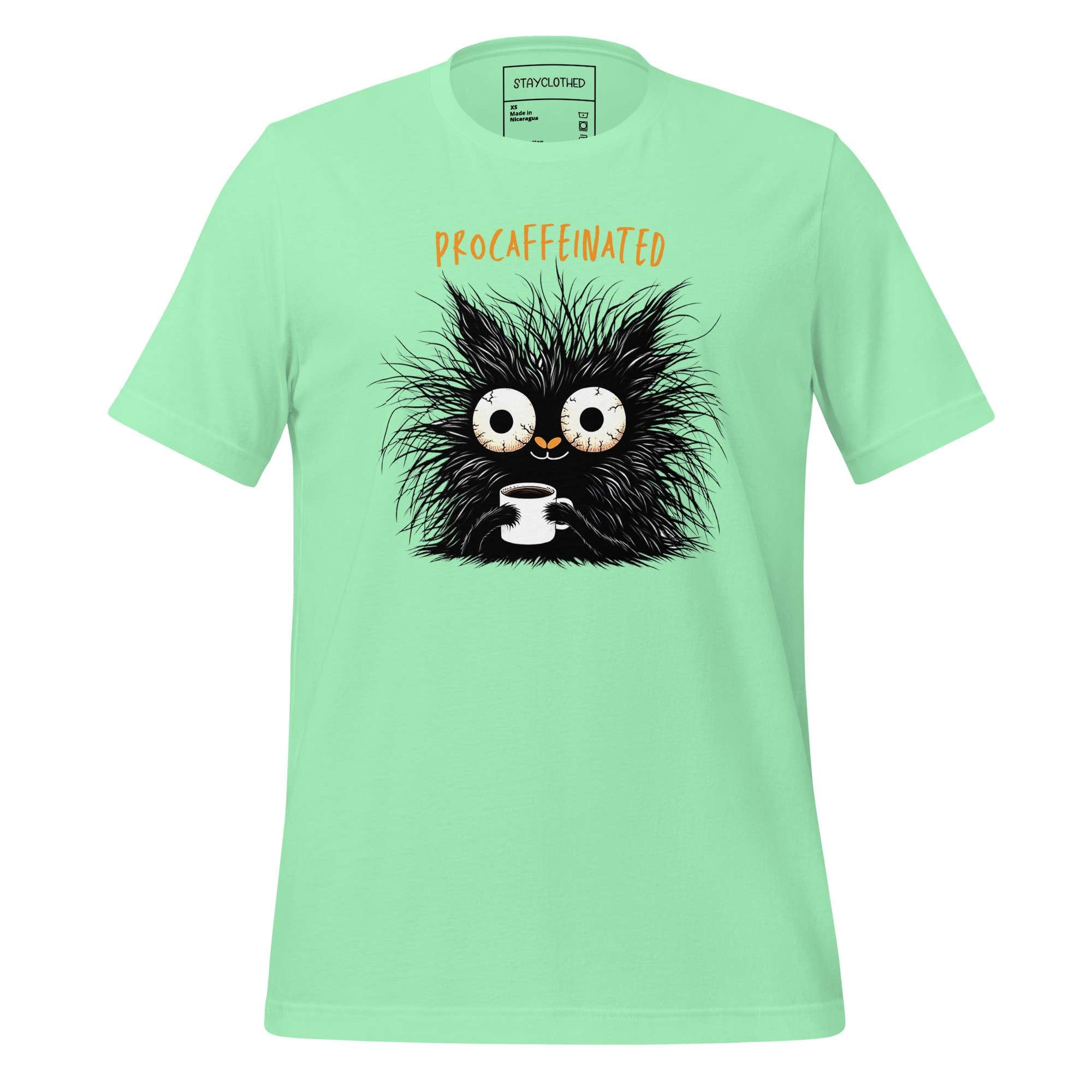 Light green t-shirt with a black creature graphic and 'DECAFFEINATED' text on a wooden surface, featuring the brand 'STAYCLOTHED'.
