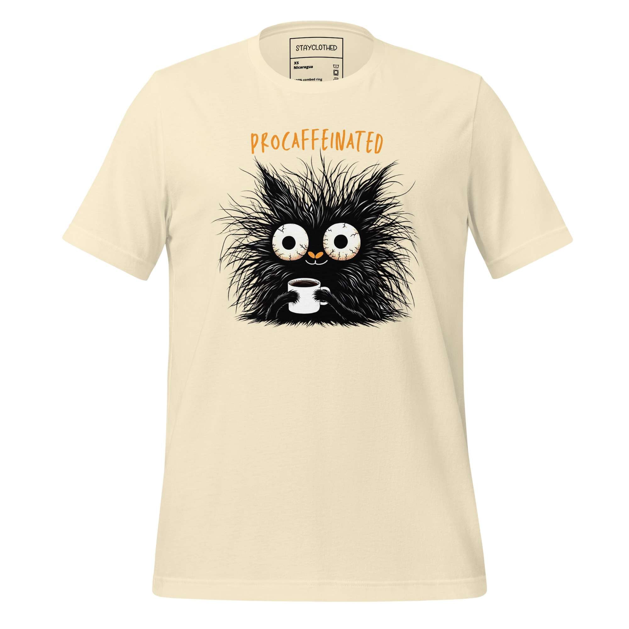 Beige t-shirt with a black creature holding a coffee cup graphic on a wooden surface, featuring the brand 'StayClothed'.