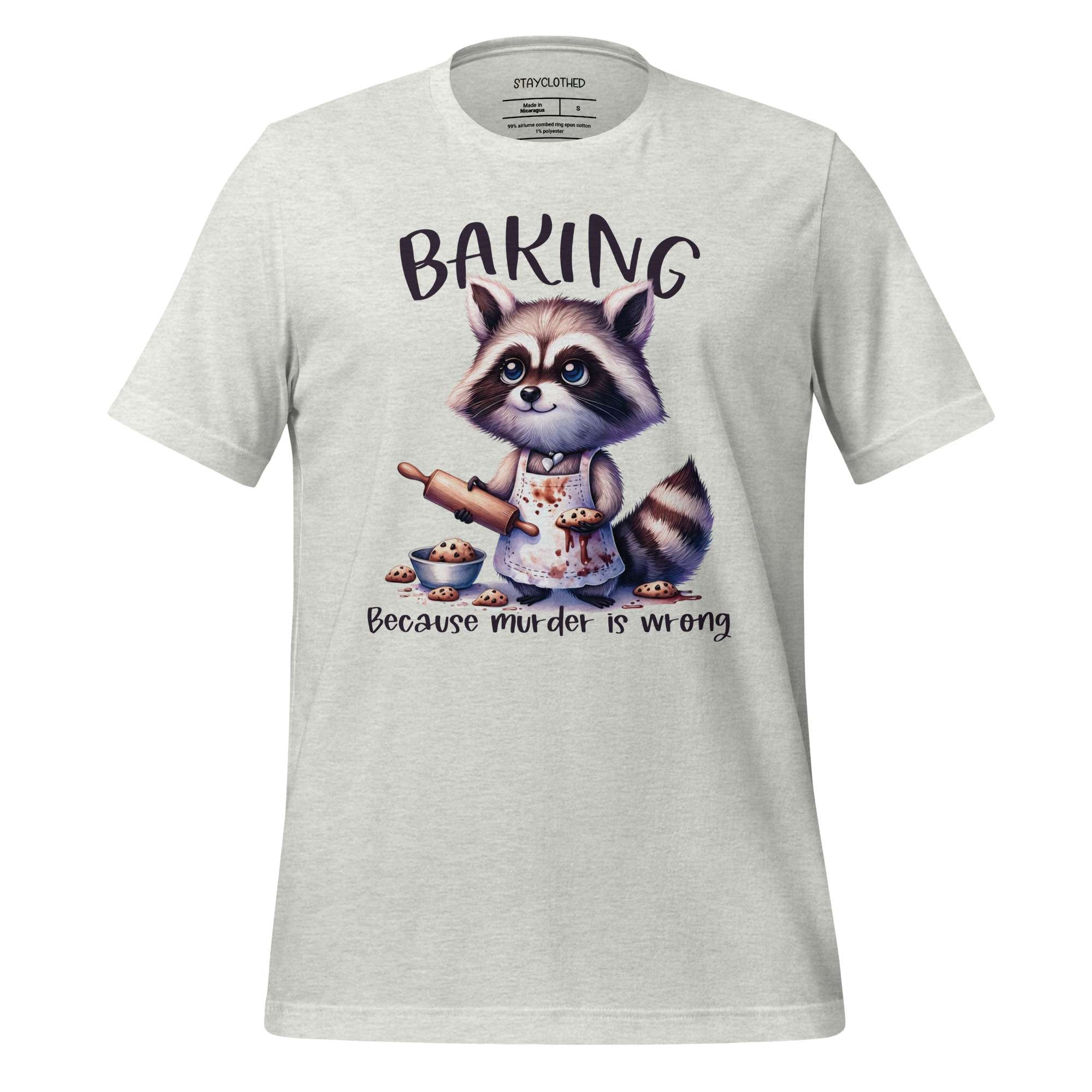 White t-shirt with a raccoon graphic and 'Baking Because Murder is Wrong' text on a wooden surface, featuring the brand 'StayClothed'.