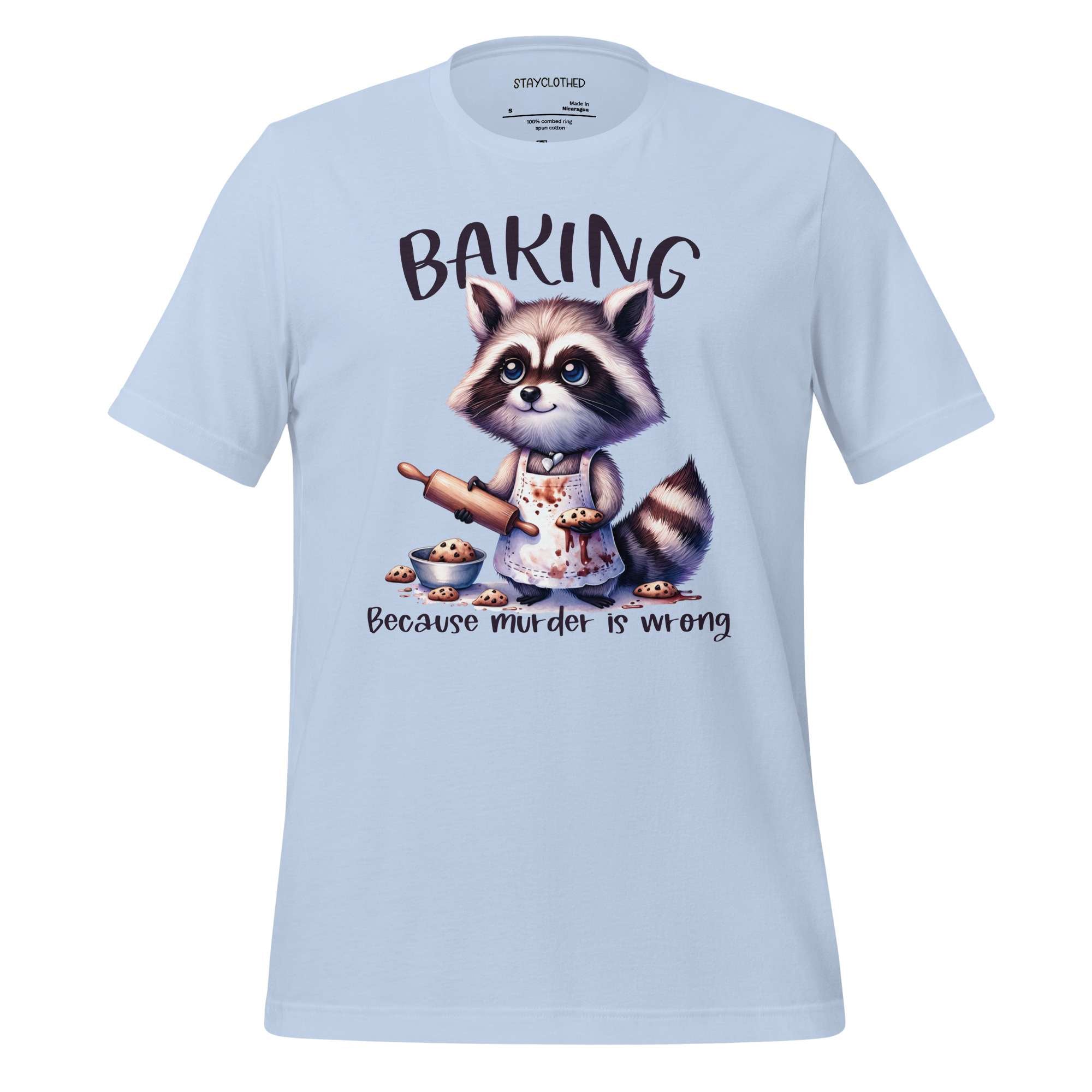 White t-shirt with a raccoon graphic and 'Baking Because Murder is Wrong' text on a wooden surface, featuring the brand 'StayClothed'.