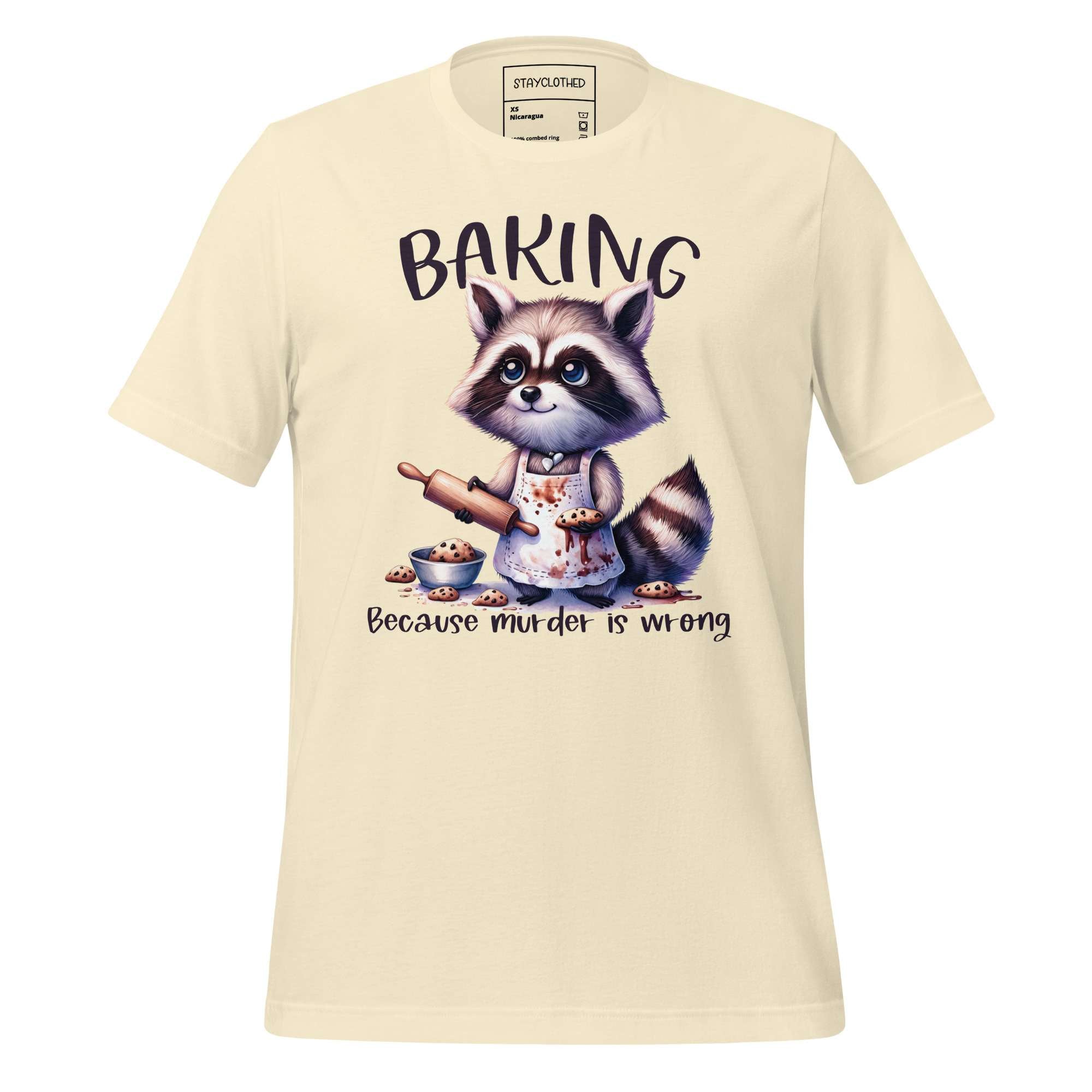 Beige t-shirt with a raccoon graphic and 'Baking Because Murder is Wrong' text on a wooden surface, featuring the brand 'StayClothed'.
