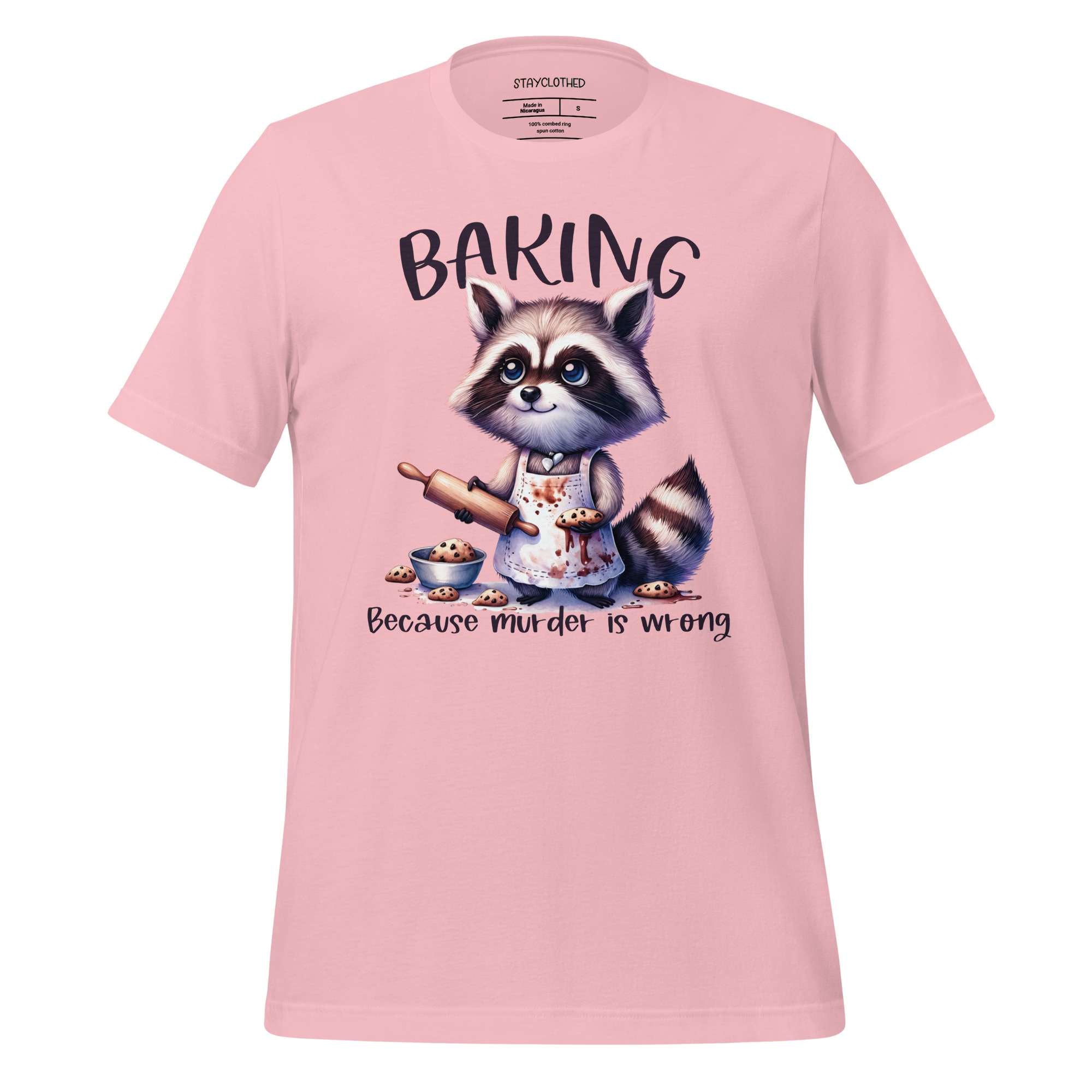Pink t-shirt with a raccoon graphic and 'Baking Because Murder is Wrong' text on a wooden surface, with 'StayClothed' branding.