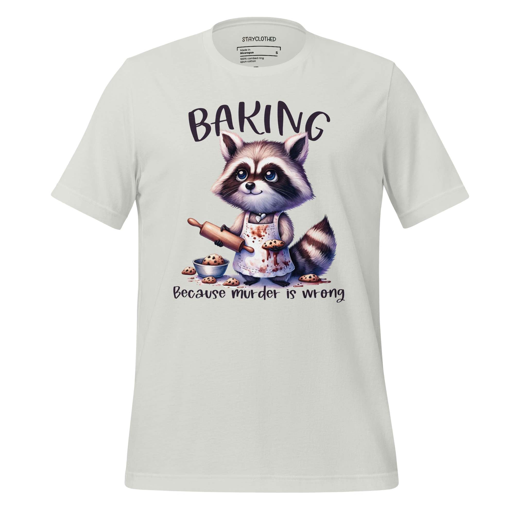 White t-shirt with a raccoon graphic and 'Baking Because Murder is Wrong' text on a wooden surface, with 'StayClothed' branding.