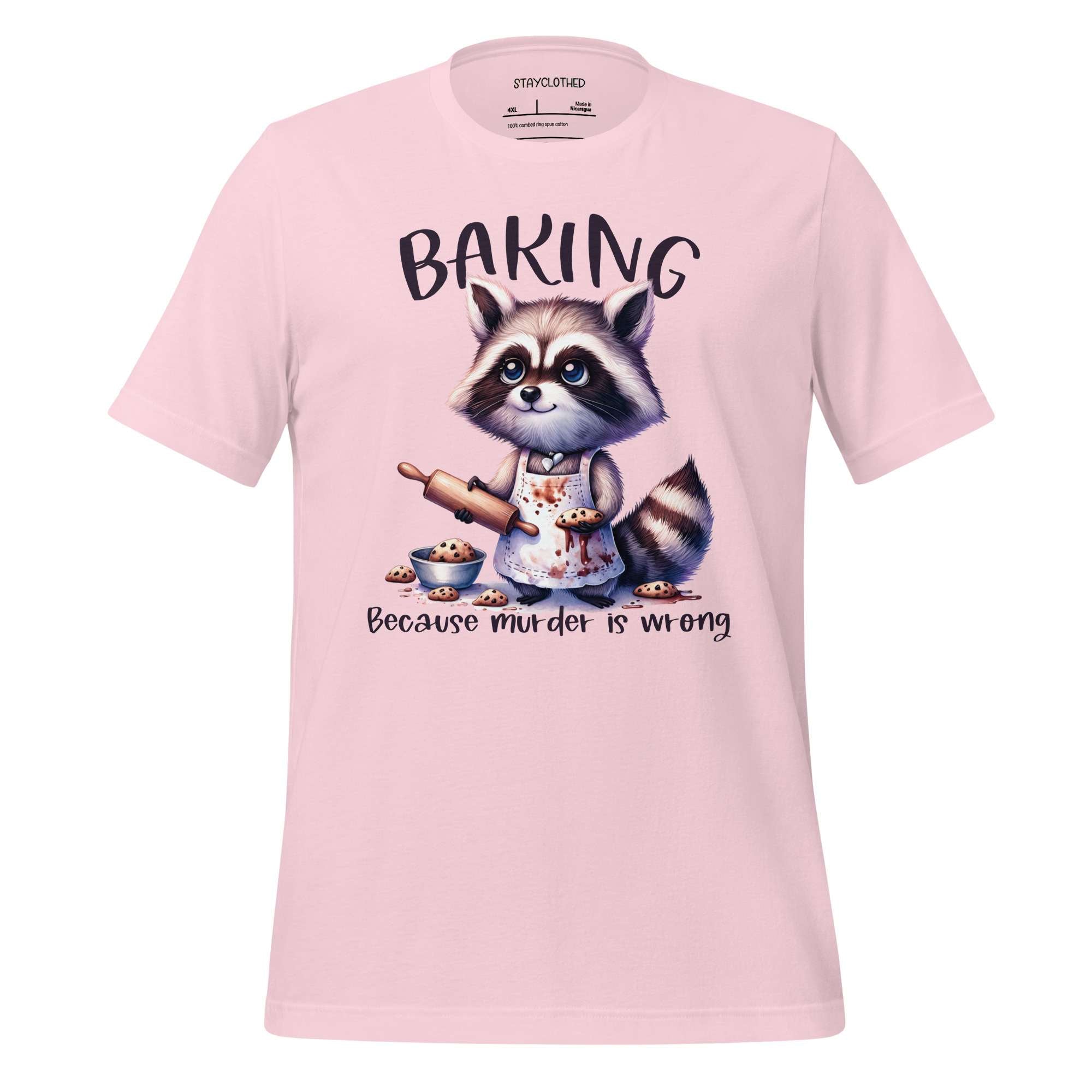 Pink t-shirt with a raccoon graphic and 'Baking Because Murder is Wrong' text on a wooden surface.
