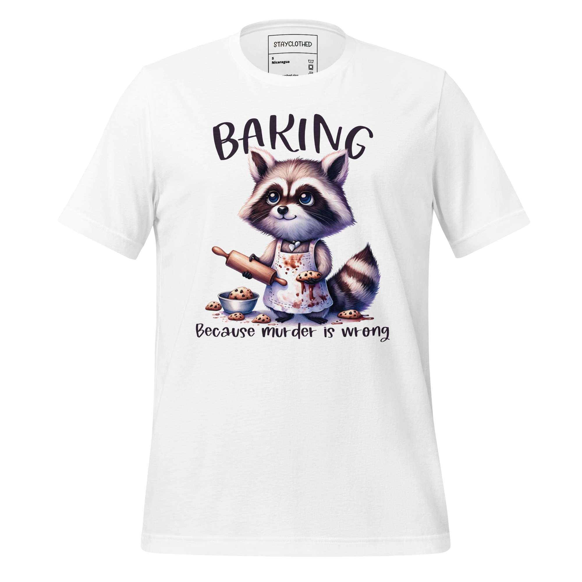 White t-shirt with a raccoon graphic and 'Baking Because Murder is Wrong' text on a wooden surface, featuring the brand 'StayClothed'.