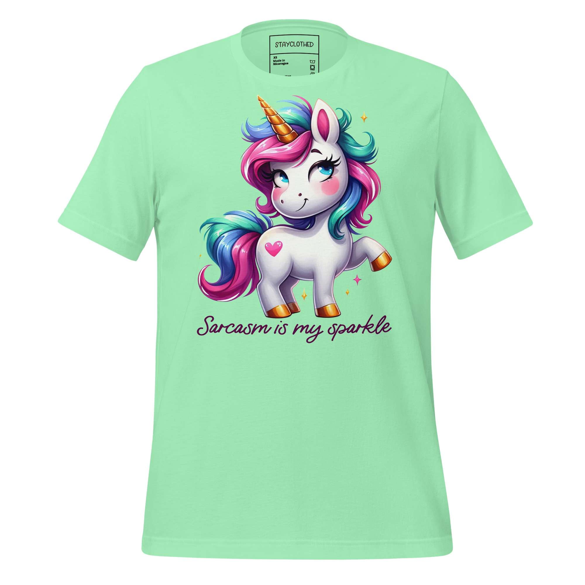 Light green t-shirt with a unicorn graphic and text on a wooden surface, featuring the brand 'StayClothed'.
