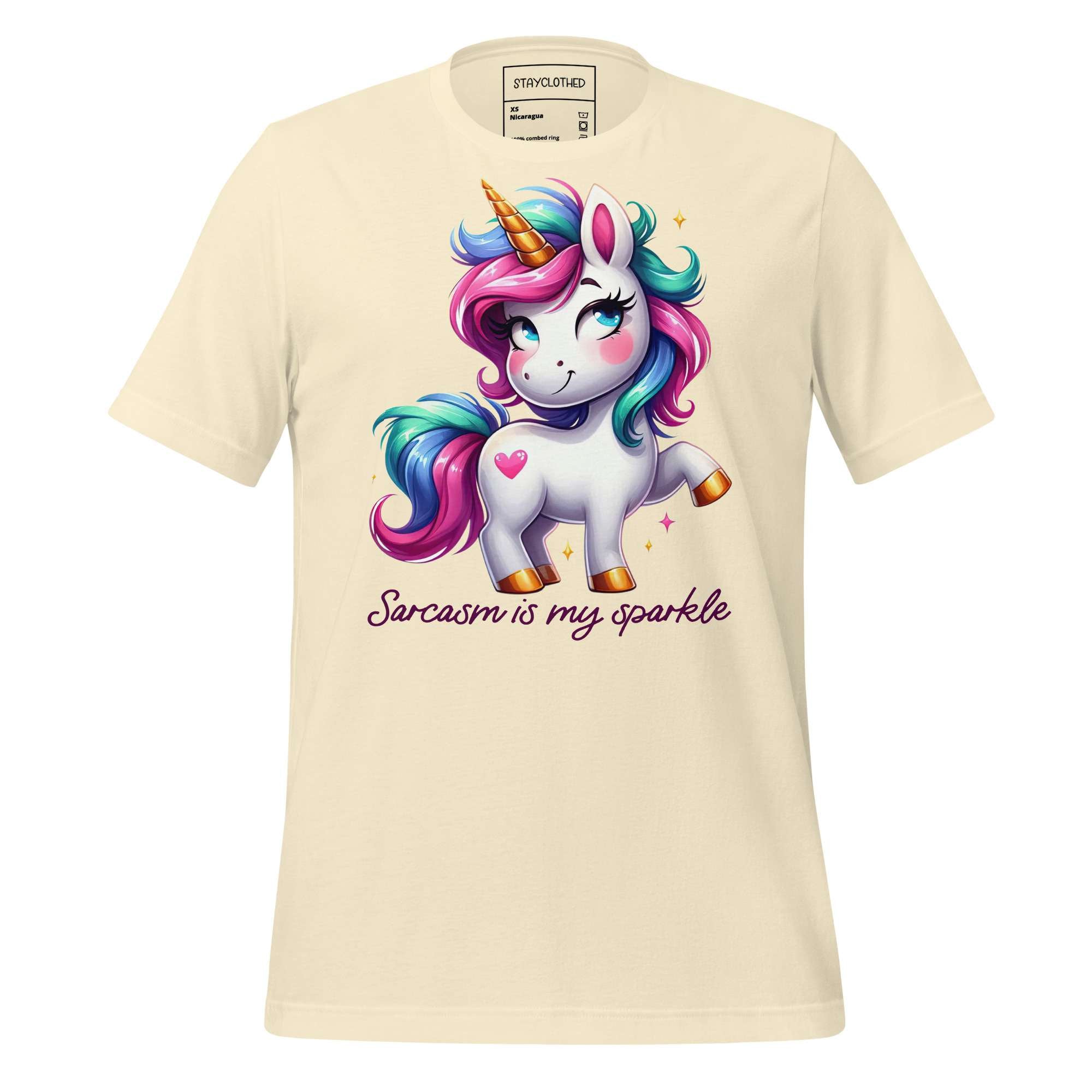 Beige t-shirt with a colorful unicorn graphic and text on a wooden surface, featuring the brand 'StayClothed'.