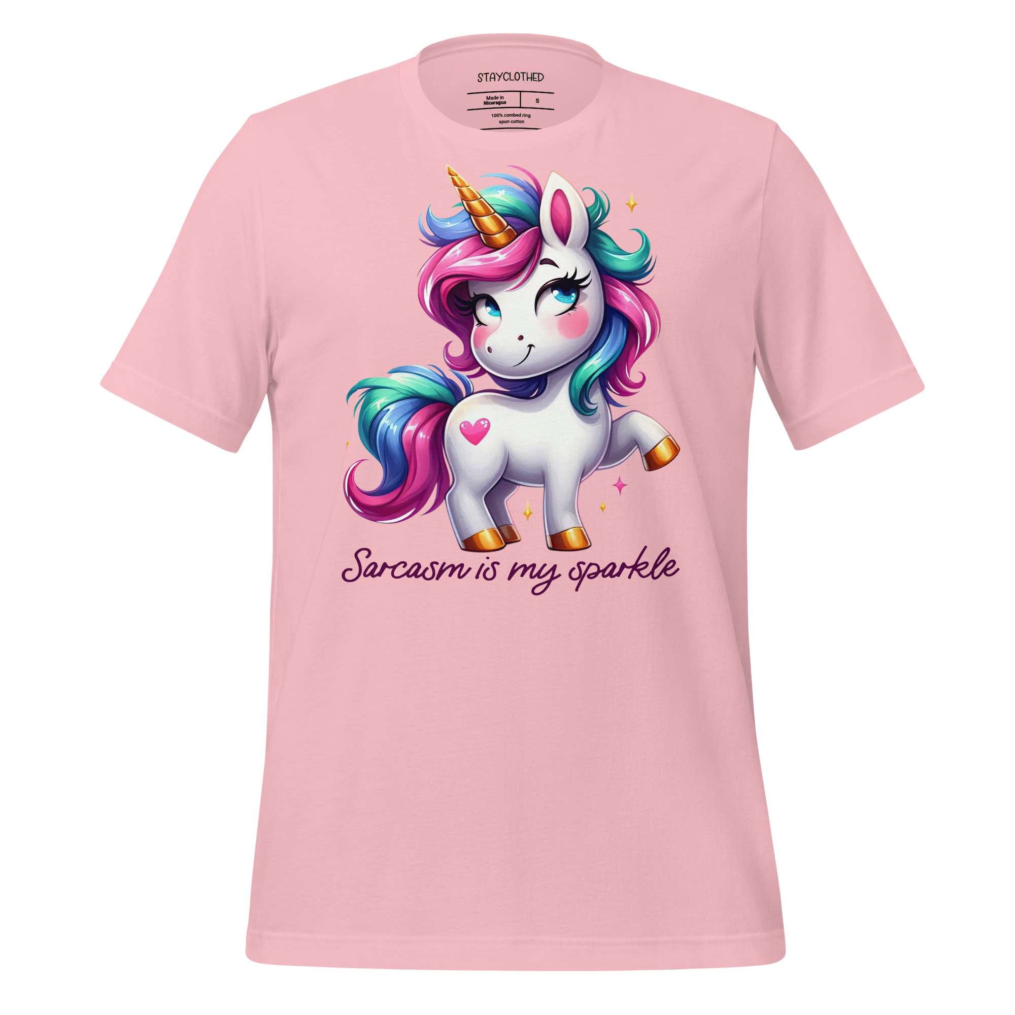 Pink t-shirt with a unicorn graphic and text on a wooden surface, featuring the brand 'StayClothed'.