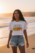 Model wearing the Stay Happy Women’s Crop Top on a beach at sunset