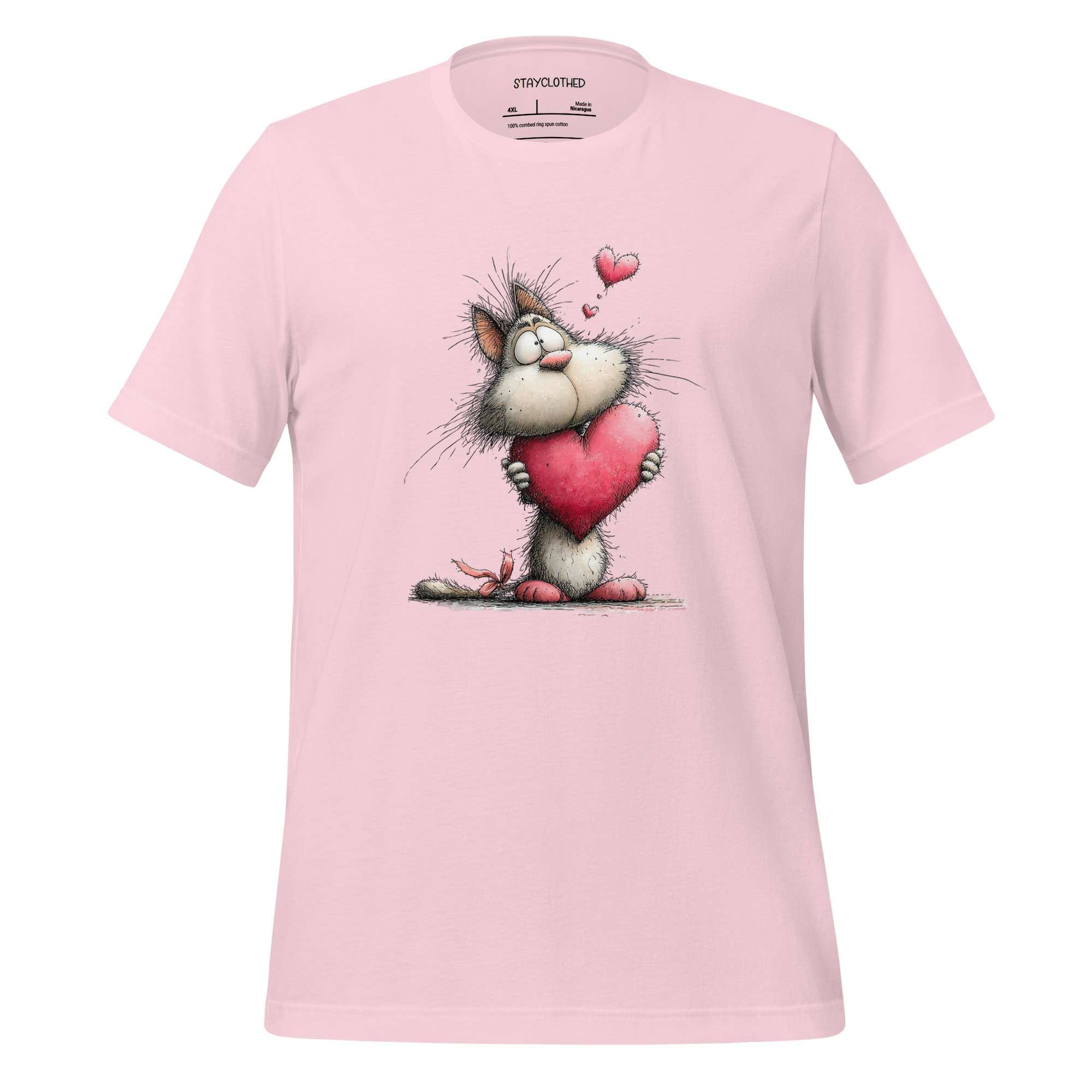 Pink t-shirt with a cartoon cat holding a heart on a wooden surface, featuring the brand 'StayClothed'.