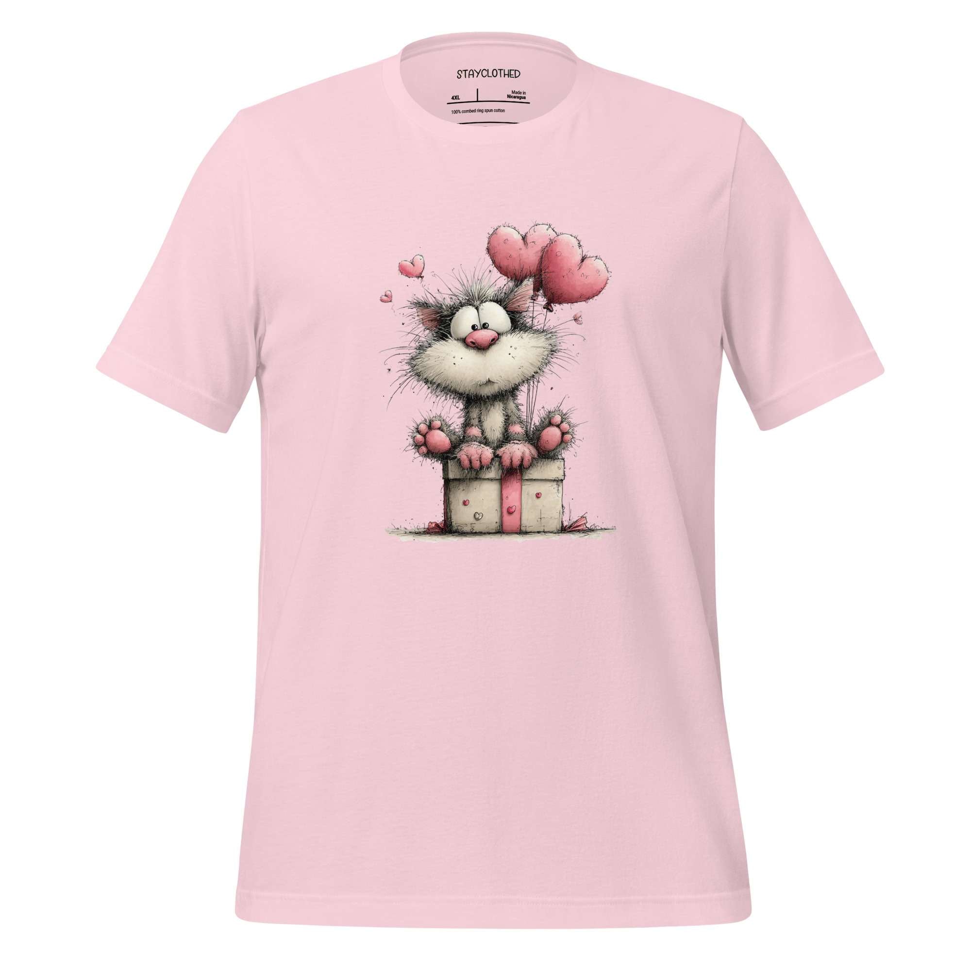 Pink t-shirt with a cartoon cat holding a gift on a wooden surface, featuring the brand 'StayClothed'.