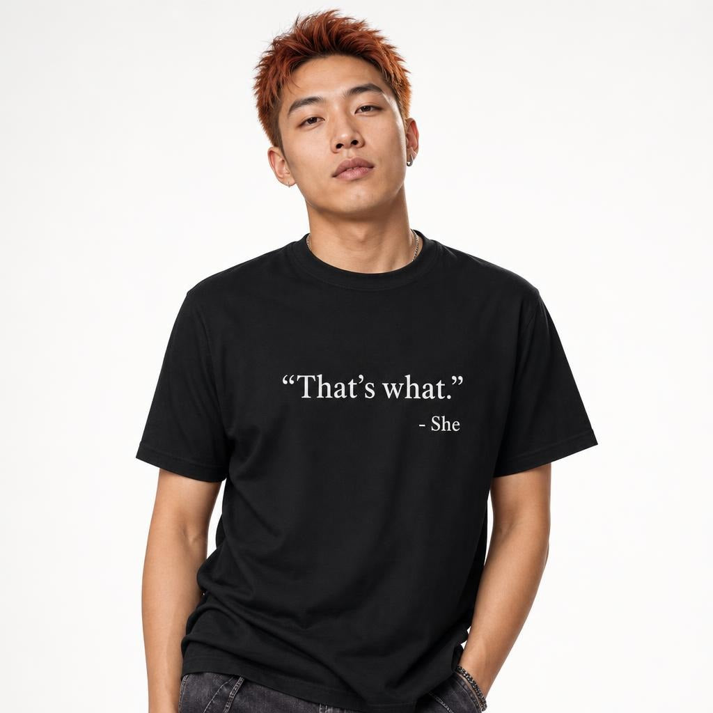 Model wearing a black T-shirt with white slogan text reading “That’s what.” and “- She” on the front.