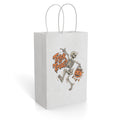 Front view of a paper gift bag with twisted handles, featuring “Trick or Treat?” beside a dancing skeleton holding a pumpkin bucket with sweets.