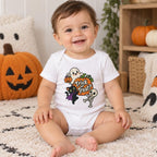 Baby wearing a white short sleeve bodysuit with “Trick or Treat?” and a cute Halloween graphic featuring a ghost, black cat, pumpkin and skeleton.
