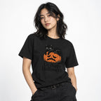 Model wearing a Black T-shirt featuring a black cat resting on a sad orange jack-o’-lantern with “Un-Happy Halloween” text.
