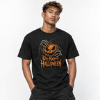 Black t shirt featuring A central orange jack-o’-lantern with an angry carved face is covered and held by skeletal hands, surrounded by twisted black vines. Distressed orange text below reads “Un-Happy Halloween”. The ar