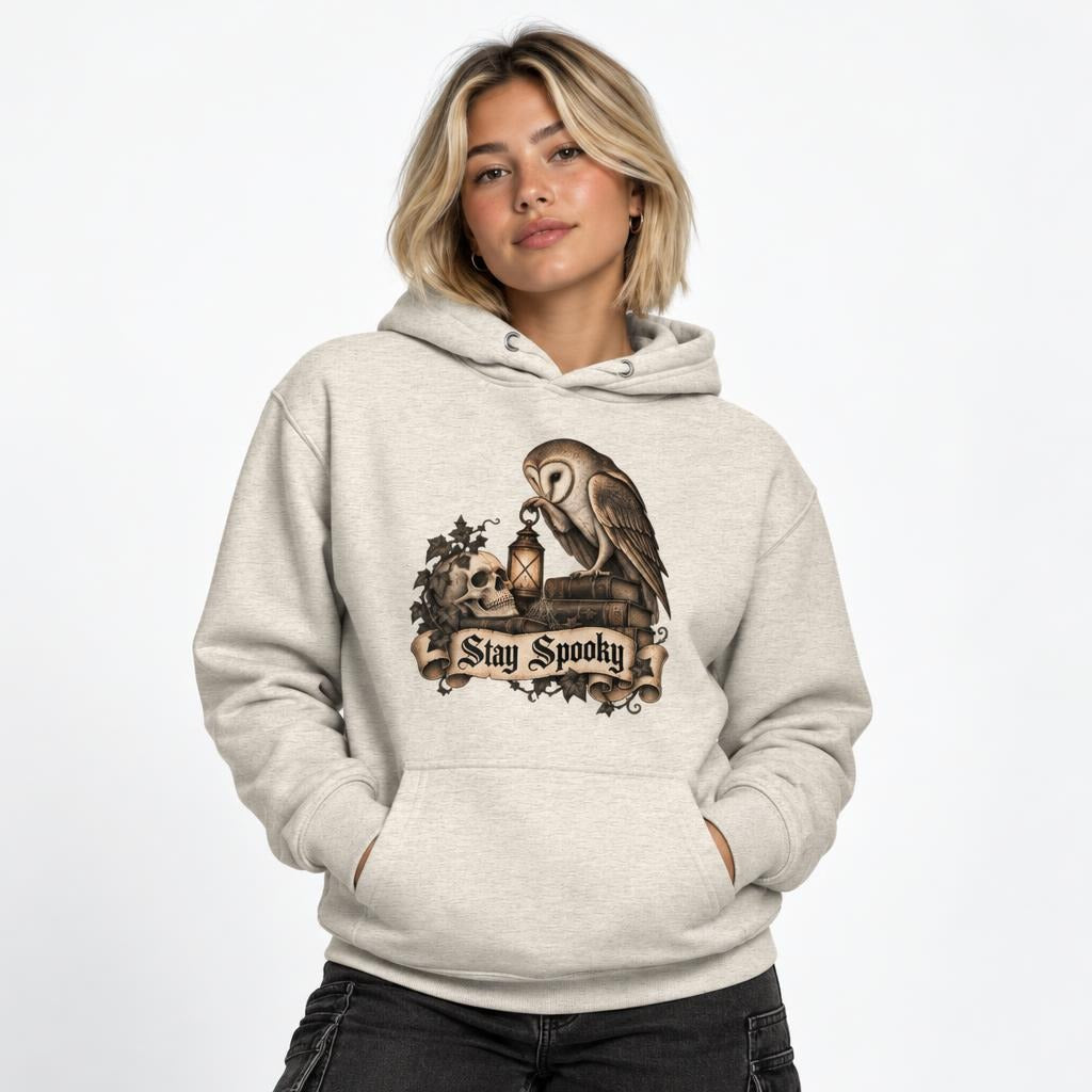 Model wearing an Oatmeal Heather hoodie featuring an owl, skull, lantern, and “Stay Spooky” artwork.