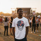Man wearing a white t-shirt with a skull design featuring an American flag and sunglasses at a music festival.