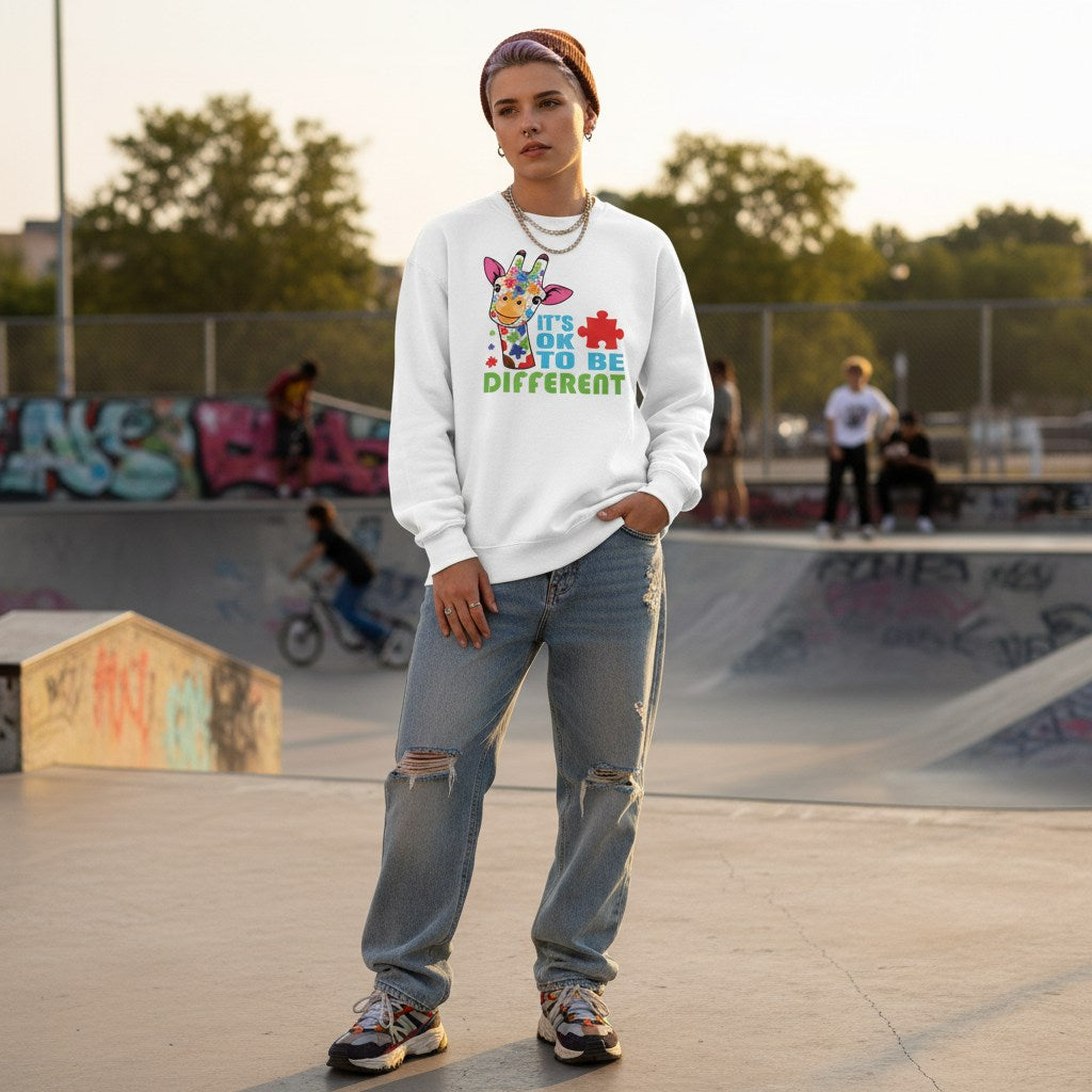 Non-binary person wearing a white "It's Okay To Be Different" autism awareness giraffe sweatshirt.