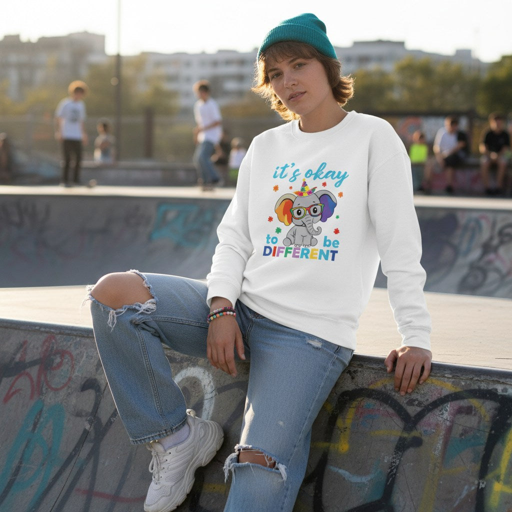 Non-binary person wearing a white sweatshirt with an elephant and the phrase Its Okay To Be Different.