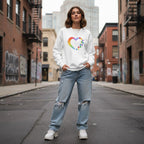 White woman wearing a white rainbow heart puzzle sweatshirt.