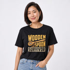 Front view of a model wearing a black T-shirt with a cartoon wooden spoon and the words “WOODEN SPOON SURVIVOR.”